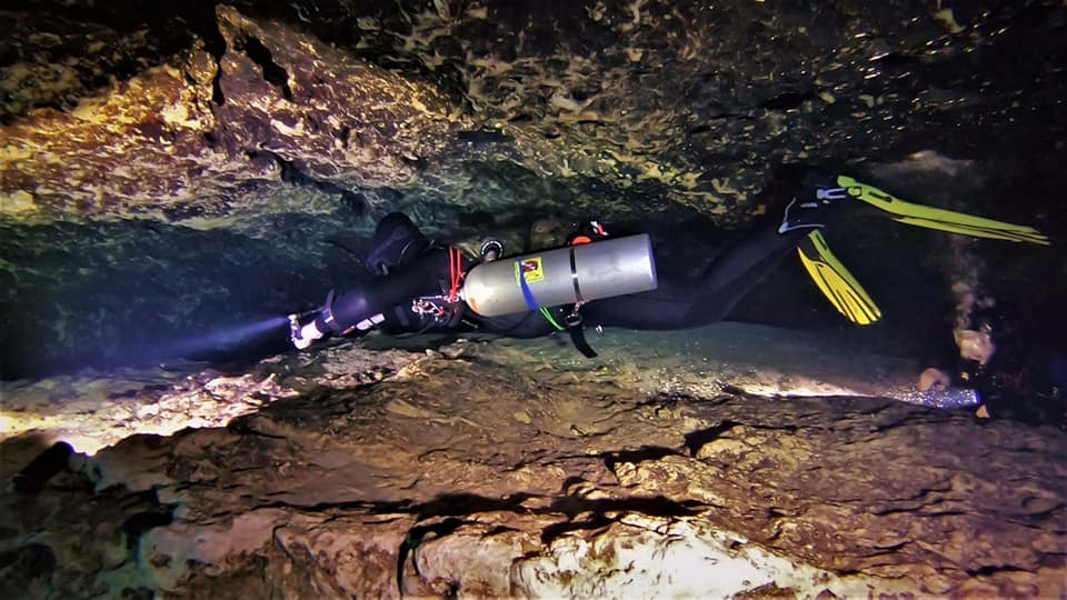 A diver with a light swimming through a low cavern passage